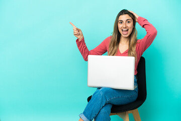 Naklejka premium Young caucasian woman sitting on a chair with her pc isolated on blue background surprised and pointing finger to the side