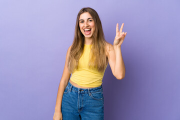 Fototapeta na wymiar Young woman over isolated purple background smiling and showing victory sign
