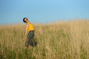 Beautiful woman in yellow shirt and long skirrt standing elegant in beige wheat field. Background of bright blue sky
