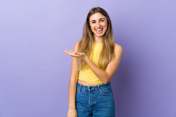 Young woman over isolated purple background presenting an idea while looking smiling towards