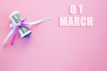 calendar date on pink background with rolled up dollar bills pinned by pink and blue ribbon with copy space. March 1 is the first day of the month