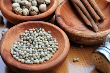 pepper, cardamom, and cinnamon in a wooden bowl on a wooden tray plus garlic and salt. close up with selective focus