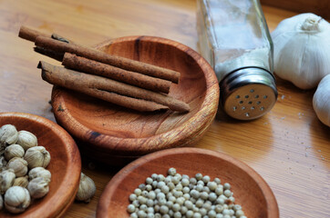 pepper, cardamom, and cinnamon in a wooden bowl on a wooden tray plus garlic and salt. close up with selective focus