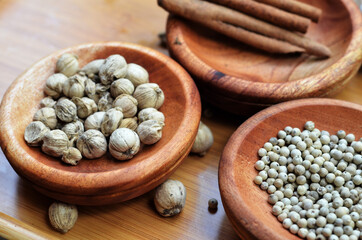 pepper, cardamom, and cinnamon in a wooden bowl on a wooden tray plus garlic and salt. close up with selective focus