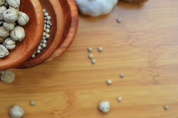pepper, cardamom, and cinnamon in a wooden bowl on a wooden tray plus garlic and salt. close up with selective focus