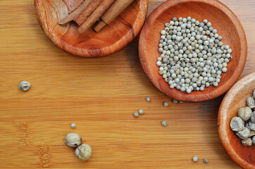pepper, cardamom, and cinnamon in a wooden bowl on a wooden tray. close up with selective focus
