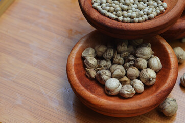pepper, cardamom, and cinnamon in a wooden bowl on a wooden tray. close up with selective focus