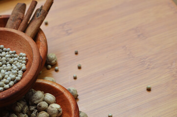 pepper, cardamom, and cinnamon in a wooden bowl on a wooden tray. close up with selective focus