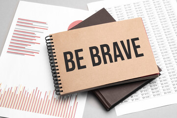 Notepad with text Be brave on a white background, near laptop, calculator and office supplies. Business concept.