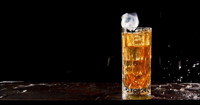 Icecube splashing to glass of cold sparkling drink. Slow motion, copy space, black background. Hard seltzer, sparkling water, aperol spritz, soft drink.