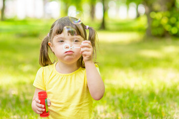 Little girl with syndrome down blows bubbles in a summer park