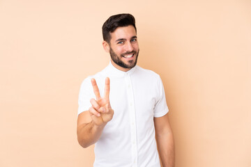 Caucasian handsome man isolated on beige background smiling and showing victory sign