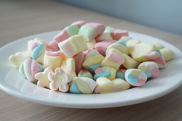 Colorful marshmallows on a white plate. Marshmallow is a type of confectionery that is typically made from sugar, water and gelatin whipped to a squishy consistency.