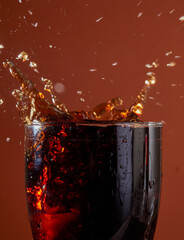 Soft drink glass with ice splash on dark background. Cola glass in celebration party concept.