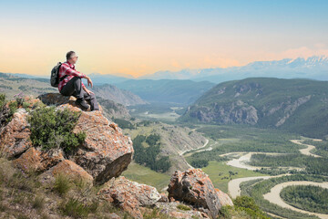  Man hiker sitting on cliff and enjoying valley view at sunset. Freedom, endless possibilities concept.