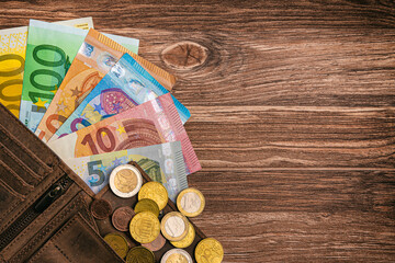 Euromünzen und Banknoten und Porte­mon­naie liegen auf einem Holztisch mit Textfreiraum - Finanzen Geld 