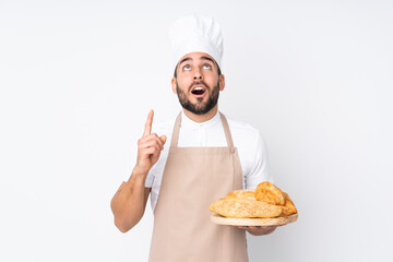 Male baker holding a table with several breads isolated on white background pointing with the index finger a great idea