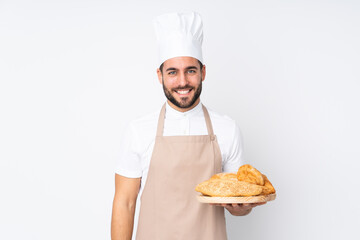 Male baker holding a table with several breads isolated on white background laughing