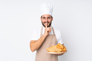 Male baker holding a table with several breads isolated on white background doing silence gesture