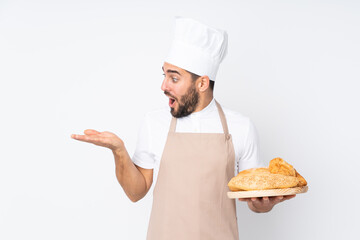Male baker holding a table with several breads isolated on white background holding copyspace imaginary on the palm