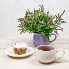 White mug of tea on a background of muffin and mint flowers on a white wooden table. Tea party with a cupcake.