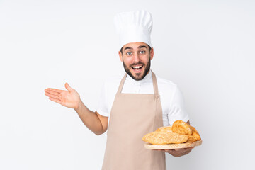 Male baker holding a table with several breads isolated on white background extending hands to the side for inviting to come