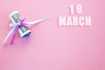 calendar date on pink background with rolled up dollar bills pinned by pink and blue ribbon with copy space. March 19 is the twenty-second day of the month