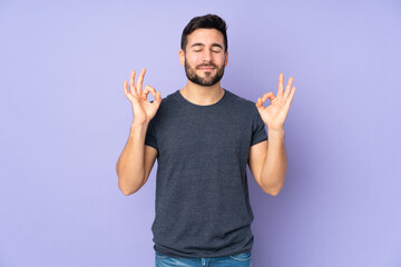 Caucasian handsome man in zen pose over isolated purple background