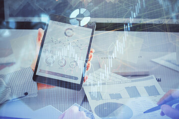 Double exposure of man's hands holding and using a digital device and forex graph drawing. Financial market concept.