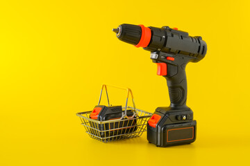 Modern black cordless screwdriver, drill with shopping basket on yellow background, copy space for text