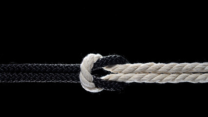Black and white ropes are tied in a knot on a black background