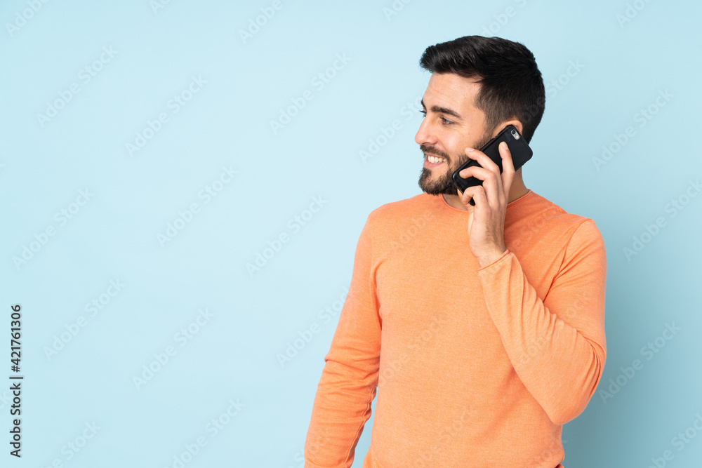 Poster Caucasian handsome man keeping a conversation with the mobile phone with someone over isolated blue background