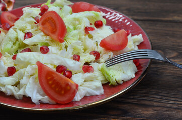 Fresh salad with peking cabbage, cherry tomato and pomegranate seeds on a ceramic plate, the concept of vegetarianism and diet