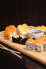 Big sushi set on light wooden dish isolated on black background