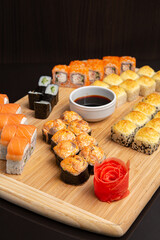 Big sushi set on light wooden dish isolated on black background