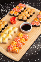 Big sushi set on light wooden dish isolated on black background