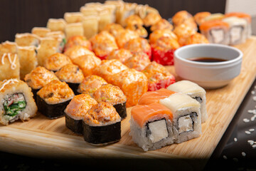 Big sushi set on light wooden dish isolated on black background