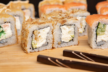 Big sushi set on light wooden dish isolated on black background