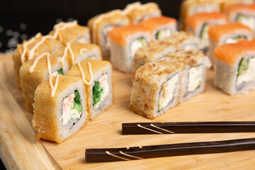 Big sushi set on light wooden dish isolated on black background
