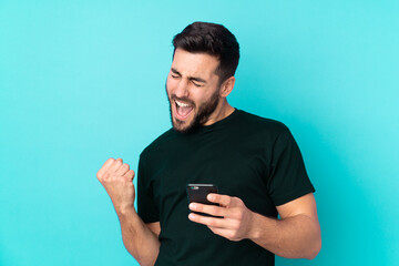 Caucasian handsome man isolated on blue background with phone in victory position