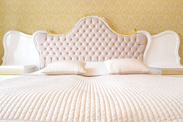 Front view of expensive bed head in italian design with two pillows and gold wall background.