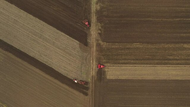 Aerial top view of three tractors, one is dragging a disc harrow and another a seedbed cultivator, third is pulling seed drill machine over arable field, soil, planting new wheat crop.