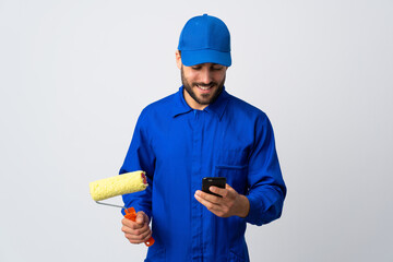 Painter man holding a paint roller isolated on white background sending a message with the mobile