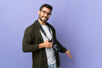 Obraz premium Photographer man over isolated purple background extending hands to the side for inviting to come
