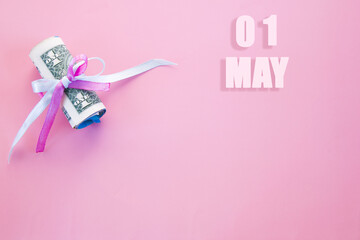 calendar date on pink background with rolled up dollar bills pinned by pink and blue ribbon with copy space. May 1 is the first day of the month