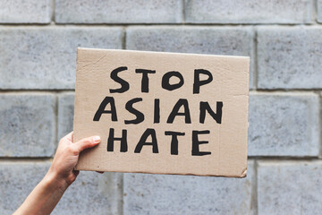 Hand holding cardboard banner with text STOP ASIAN HATE. Asian is not virus. Anti-racism protest....