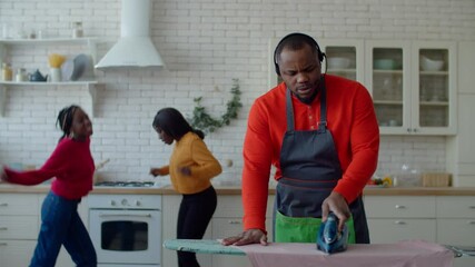 Multitasking housekeeping black single father in headset doing household chores, ironing clothes, dealing with business problems on phone and scolding naughty teenage daughters for misbehavior indoors