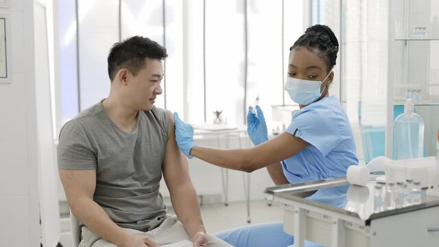 Crop view of female nurse in protective mask disinfecting patient shoulder vaccinating male patient, putting stamp on document and shaking his hand . Concept of vaccination program.