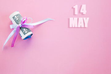 calendar date on pink background with rolled up dollar bills pinned by pink and blue ribbon with copy space. May 14 is the fourteenth day of the month