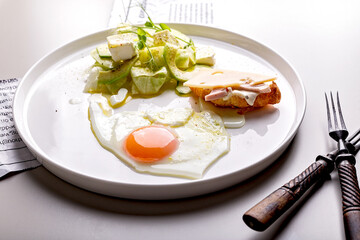 Delicious and healthy breakfast. Fried egg and vegetable salad with avocado and herbs. Mini croissant with ham and cheese on a round white plate. Organic food